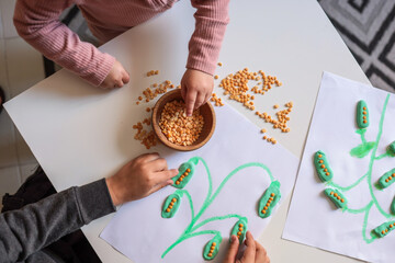 Children’s hands playing with dry lentils and modeling clay, creating a plant-themed craft on...