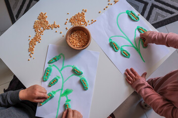 Children’s hands playing with dry lentils and modeling clay, creating a plant-themed craft on paper. A fun educational activity involving tactile learning and creativity
