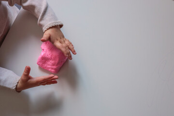 Small child squeezing soft pink modeling clay on a white table. Close-up of hands engaged in...