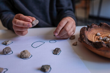 Child sorting small natural stones onto drawn circles on white paper. Educational and sensory...