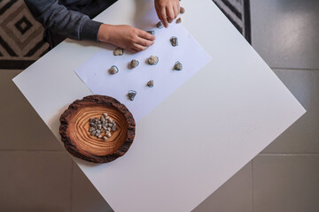Child sorting small natural stones onto drawn circles on white paper. Educational and sensory...