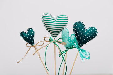 Handmade textile hearts on sticks decorated with bows made of jute and ribbon. Soft toy ornaments with polka dot and striped patterns on a white background.