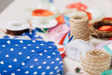 Colorful sewing and crafting supplies on a table, including lace, twine, satin ribbons, and blue fabric with white heart pattern. Close-up of materials for handmade and DIY projects.