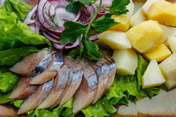 Traditional dish with sliced salted herring, boiled potatoes, and red onion, served on fresh lettuce and garnished with parsley. Classic Eastern European appetizer.