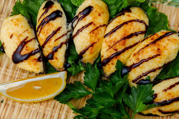 Close-up of baked mussels with cheese and sauce, served on a bed of lettuce with fresh parsley and a slice of lemon. Traditional Japanese seafood dish presented on a bamboo mat.