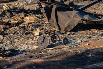 Charred remains of a tricycle among debris after a fire. The scorched ground and burnt objects symbolize destruction, loss, and the aftermath of a disaster