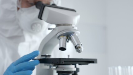Scientific researcher wearing blue protective gloves fine tuning microscope lenses during medical...