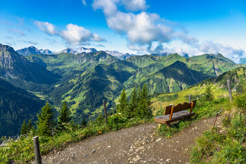 wooden park bench on mountain foot path with interesting panoramic view to the rocky mountains from Vorarlberg. the mountain Aries stone behind, interesting sky with waves clouds