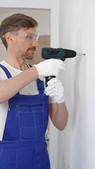 Professional male construction worker in a blue jumpsuit, safety goggles, and work gloves is...