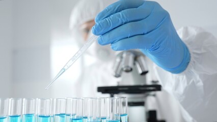 Scientific researcher wearing protective equipment, carefully pipetting liquid into test tubes...