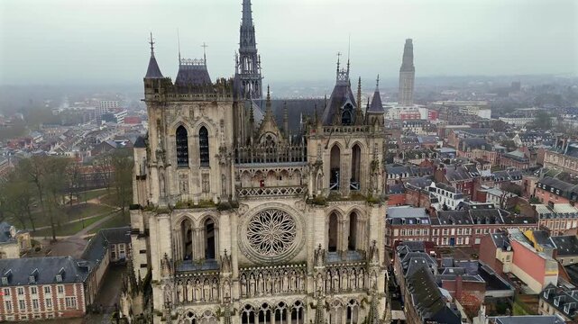 Drone view of Amiens Cathedral from the front showcasing its majestic Gothic facade with detailed rose window twin towers and the surrounding urban landscape of northern France 