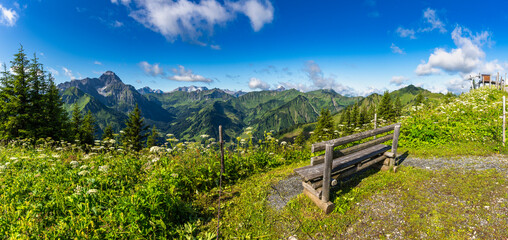 wooden park bench on mountain foot path with interesting panoramic view to the rocky mountains from Vorarlberg. the mountain Aries stone behind, interesting sky with waves clouds