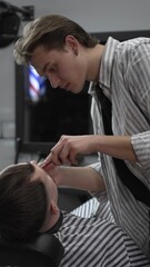 Professional barber trimming customer's hair with electric clipper, focusing on precise nape...