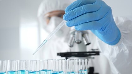 Scientific researcher wearing protective equipment, carefully pipetting liquid into test tubes...
