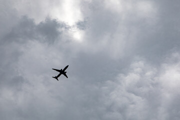 Dark airplane silhouette flying through dramatic cloudy overcast sky
