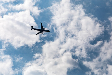 Airplane silhouette flying through blue sky with white fluffy clouds