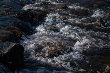 The river rushed over the rocks, creating a spray of mist in the bright sunlight. The spray...