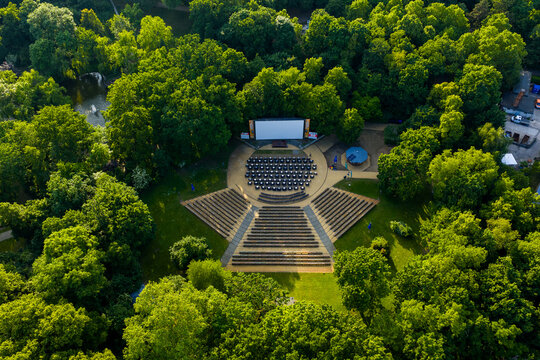 Aerial view of an open-air amphitheater nestled among lush green trees, a stage set against the backdrop of nature's vibrant hues, Friedrichshain-Kreuzberg, Berlin, Volkspark Friedrichshain, Germany.