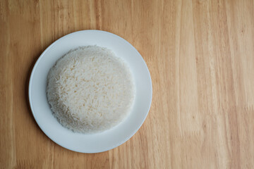 flat lay top view shot of streamed white Thai's jasmine rice in the white clean dish isolated put on the wooden plate dinner table closed to one conner of the photo with empty copy space for texts