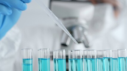 Scientific glassware containing blue solution, researcher carefully dispensing liquid via pipette...