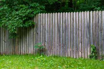 old weathered wooden fence against the background of green lawn and forest beautiful rural landscape