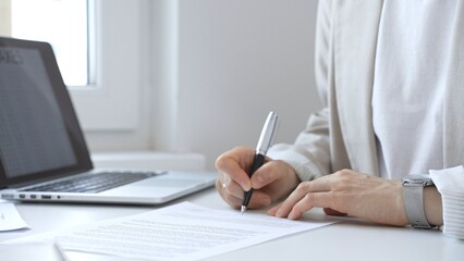 Businesswoman signing a contract at her office desk, surrounded by a laptop and documents,...