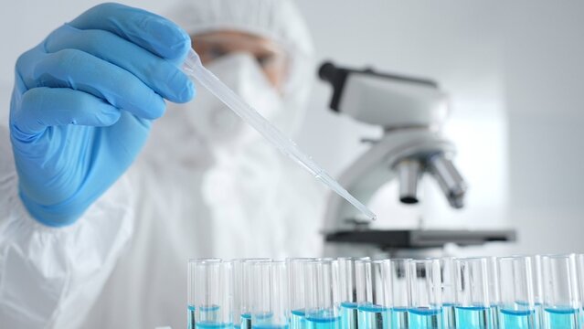 Scientific researcher wearing protective gear, carefully pipetting liquid into test tubes while conducting medical research experiment in laboratory. Medicine, healthcare and science concept