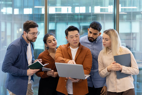 A diverse team collaborates around a laptop in a modern office setting, brainstorming ideas and strategies.