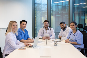 A diverse group of medical professionals are seated around a conference table, appearing to be discussing and collaborating.