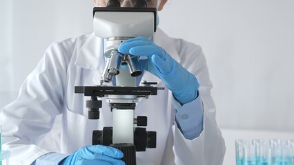 Female scientist wearing protective gear carefully adjusting microscope lens, analyzing medical...