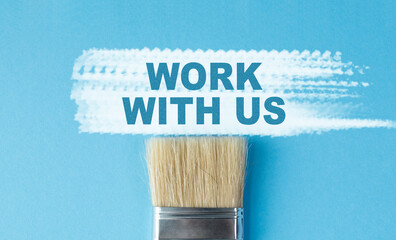 A paintbrush with the word Work With Us written on it. The brush is on a blue background