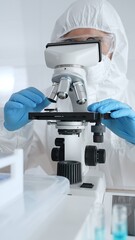 Scientific researcher wearing protective gear adjusting microscope, analyzing lab samples with...