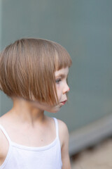 A little girl with a stylish bob hairstyle is wearing a cute white tank top that adds to her adorable look and brings out her charm