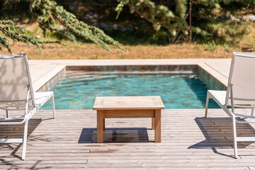 Cozy wooden deck with pool and sun loungers under pine trees

