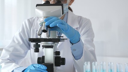 A female scientist in protective gear adjusts a microscope lens and accurately analyzes medical...