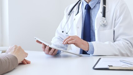 Close-up of doctor man showing information on tablet to patient woman during medical visit,...