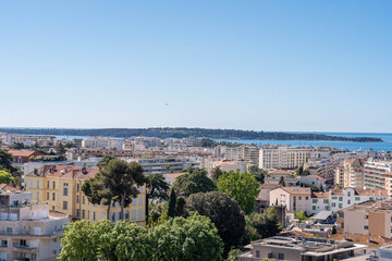 Obraz premium Aerial view of Cannes city rooftops with greenery and distant Lérins Islands under bright blue sky on the French Riviera