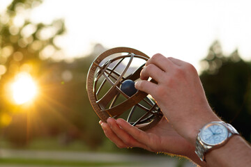 Close-up of hands holding antique globe at sunset outdoors. Armillary sphere on hand, spherical...