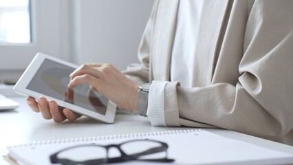 Professional woman working on digital tablet at the desk, checking digital content with notebook...