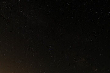 Several meteors from a summer shower streak across the Milky Way in a wide long-exposure image,...