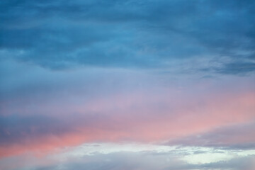 Large dark blue cloud with blue-pink glows creeping over the bright horizon, mystical clouds in the evening light, blurred background, soft focus.