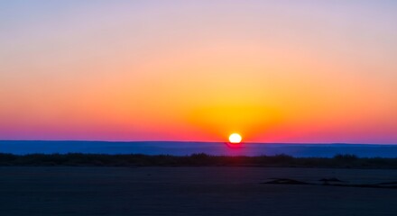 A vibrant sunset over the ocean with a gradient sky and dark land in the foreground view