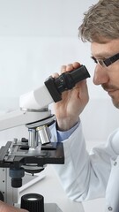 A male scientist looks through a microscope in a brightly lit laboratory while conducting research...