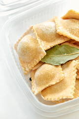 A Close-Up View of Freshly Made Ravioli in a Clear Container with a Bay Leaf Garnish, Showcasing Their Texture and Shape Perfectly.