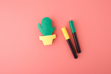 Unfinished paper cactus in yellow pot next to green and yellow markers on pink background. DIY...