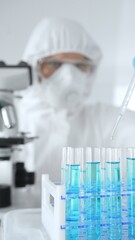 Scientific researcher wearing protective gear, carefully pipetting liquid into test tubes while...