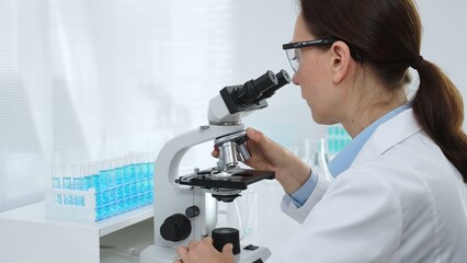 Female scientist examining microscope slide, analyzing chemical sample in sterile laboratory...