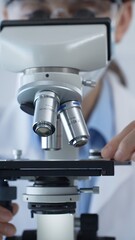Female scientist wearing lab coat and protective glasses using a modern microscope in a laboratory...