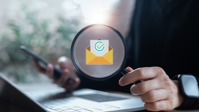 Hand holding magnifying glass focusing on email with checkmark icon, symbolizing email verification, secure communication, and digital identity.