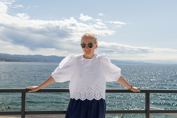 Young woman enjoying a sunny day by the waterfront, wearing sunglasses and a stylish outfit,...